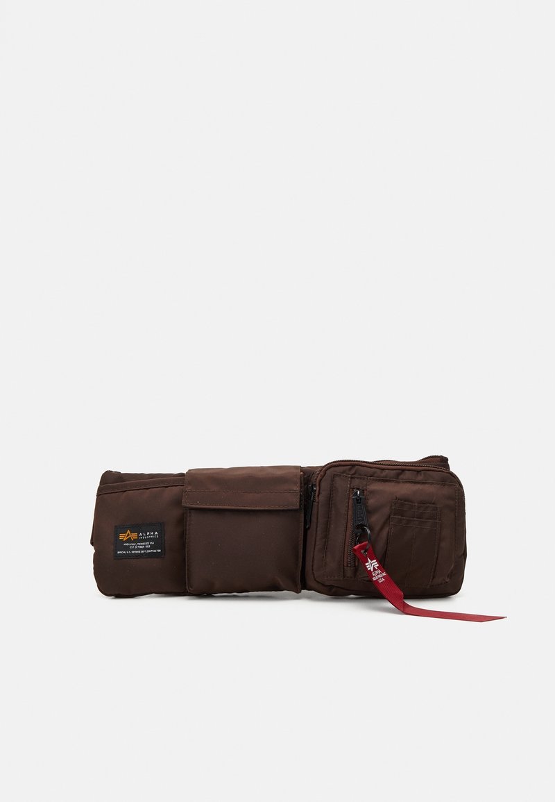 Sac banane marron avec trois compartiments, dont un zippé avec une languette en tissu rouge, présenté sur fond blanc.