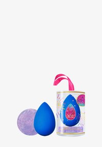 Een blauwe make-up spons met een textuur en ronde vorm. Vergezeld van een glinsterende paarse schijf en verpakt in een cilindrische, versierde houder.