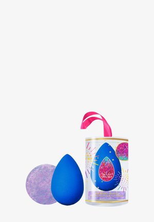 Éponge à maquillage bleue avec une forme ronde texturée. Accompagnée d'un disque violet pailleté et logée dans un conteneur cylindrique décoré.