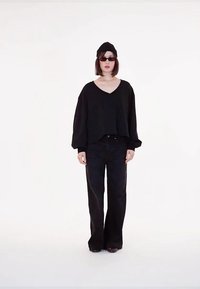 Melnā pārāk liela V veida kakla blūze ar brīvām piedurknēm, apvienota ar augsto vidukli melnām platām biksēm. Aksesuāri ietver melnu beatu un saulesbrilles.