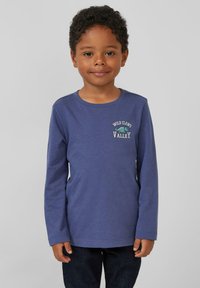 Paarse langsliavende shirt met een ronde halslijn, voorzien van een geborduurd dinosauruss ontwerp en tekst op de borst, gecombineerd met donkere jeans.