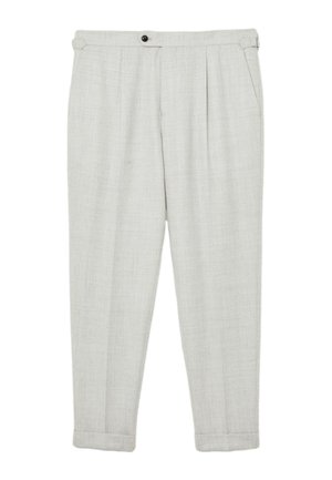 Hand in de zak van lichtbeige gestructureerde broek met zijgesp, gecombineerd met een mouw van een grijze kabelgebreide trui met witte strepen.