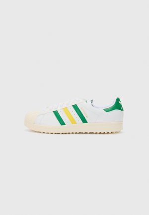 Sneaker bianche basse con strisce verdi e gialle, punta a guscio in gomma e suola testurizzata color crema. Marchio sul tallone e sulla linguetta.