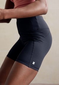 Pantaloni sportivi neri con vita alta, realizzati in materiale elasticizzato e aderente. Presentano cuciture discrete e un piccolo logo vicino all'orlo.