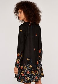 Svart klänning med långa ärmar som har färgglad blomm- och fjärilsbroderi längs fållen och axlarna. Mjuk tyg med en flödande design.