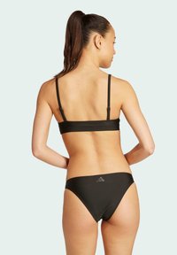 Černý bikiny top s tenkými ramínky, který má nastavitelné zavírání vzadu; odpovídající bikiny spodní díl s nízkým pasem a akcentem loga.