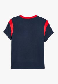 Camiseta de manga corta azul marino con acentos rojos en los hombros y el cuello, hecha de una tela suave con una textura lisa y un corte regular.
