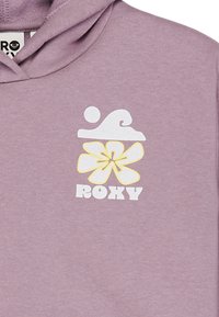 Fialová mikina s bílým grafickým motivem vlny a květiny, s nápisem "ROXY" v tučných písmenech pod designem. Měkká, texturovaná látka.