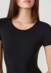 Bodysuit noir à manches courtes avec un col rond, fabriqué à partir d'un matériau lisse et extensible, au design ajusté avec des coutures minimales.