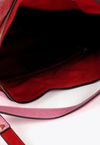 Částečně otevřená kabelka odhaluje červený vnitřek a černé podšívku. Taška má růžovou rukojeť a zip na vrchu.
