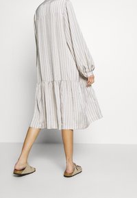 Pruhované šaty s dlouhým rukávem a volánkovým lemem, vyrobené z lehké látky v pastelových barvách. Nosit s otevřenými sandály, které ukazují holé nohy.