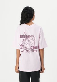 Růžové bavlněné tričko s krátkými rukávy, na kterém je velká grafika jahody a text „A BERRY GOOD time“ v tmavě burgundské barvě.