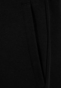 Schwarz Sweatshirtstoff zeigt eine glatte Textur mit einem seitlichen Taschendetail. Das Material scheint dick und weich zu sein, mit sichtbaren Nähten an den Kanten.