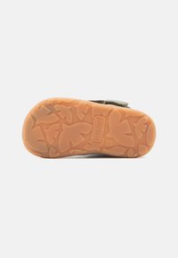 Kinderschuhe mit einer strukturierten Gummisohle mit Blattmustern, in hellbrauner Farbe und einem Oberschuh aus Wildleder mit einem Riemenverschluss.