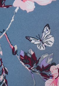 Tejido con un fondo azul, decorado con patrones florales multicolores y una mariposa blanca. El diseño incluye flores rosas y moradas.