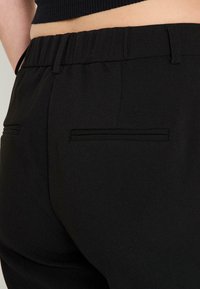 Pantalones de chándal negros que muestran la cintura elástica, bolsillos laterales con un acabado elegante y una tela texturizada sin patrones visibles.
