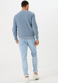 Blauwe geribbelde trui met lange mouwen, ronde halslijn en textuurpatroon, gecombineerd met lichtblauwe jeans en witte sneakers.
