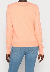 Persika tröja i mjukt stickat material med ribbade ärmslut och nederkant, med en klassisk rund hals och avslappnad passform, ihop med ljusblå jeans.