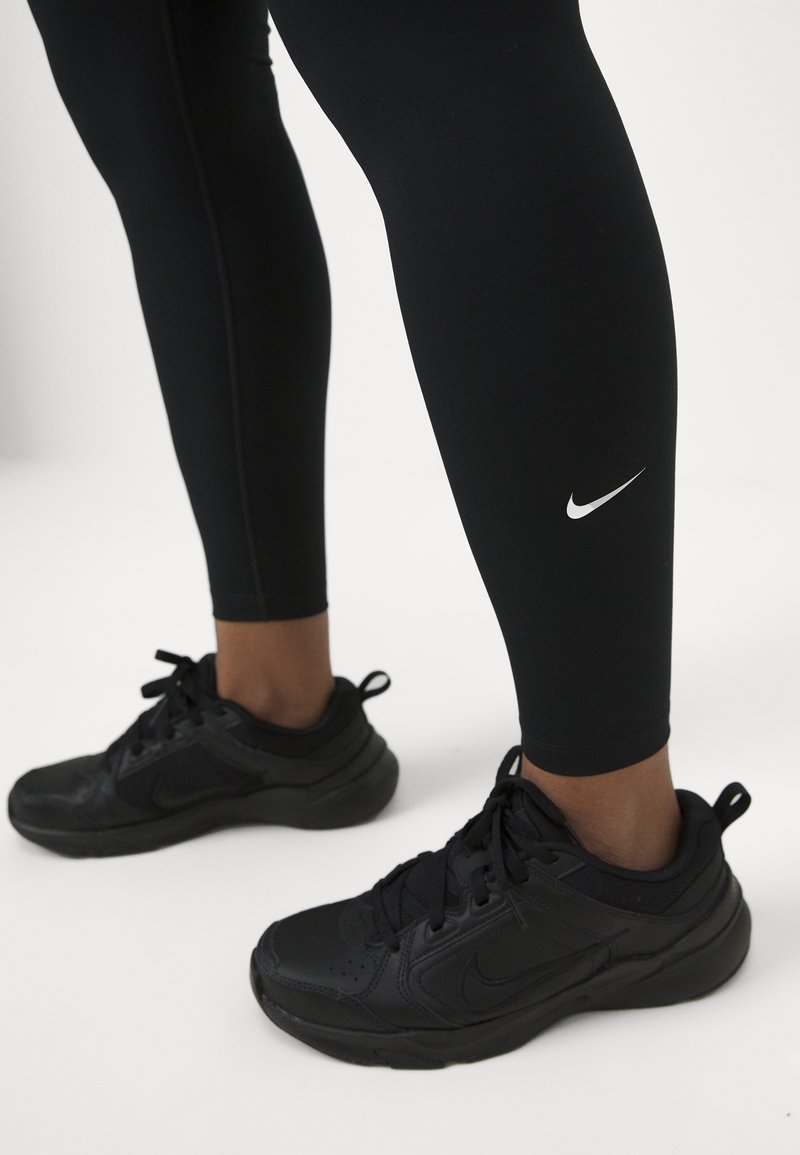 Leggings sportivi neri con un design aderente e un piccolo logo Nike bianco. Abbinati a scarpe da ginnastica nere con una superficie testurizzata e lacci.
