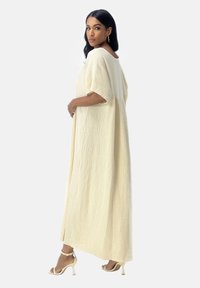 Roomkleurige, gestructureerde maxi-jurk met korte mouwen, een ontspannen pasvorm en een detail met zijdelingse plooien, gecombineerd met naakte sandalen met hak.