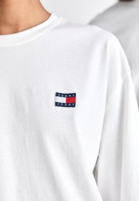 Witte longsleeve t-shirt van katoen, met een klein navy en rood Tommy Jeans logo op de borst. Zachte textuur, ruime pasvorm.