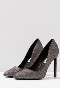 Pompes à talons hauts en argent pailleté avec des pointes aiguisées et un design épuré. Intérieur noir lisse et talons aiguilles de 10 cm.
