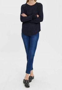 Maglione lavorato a maglia di un blu navy scuro con un motivo testurizzato, scollatura rotonda e polsini a costine, abbinato a jeans blu aderenti e mule nere con tacco a blocco.