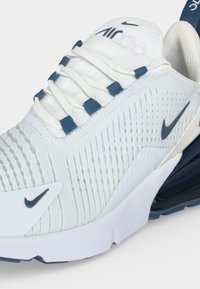 Άσπρο και ναυτικό μπλε αθλητικό παπούτσι Nike Air Max 270 με λεπτομέρειες στο πλάι, υφασμένο πάνω μέρος, κορδόνια με ναυτικό μπλε οφθαλμούς και ορατή σόλα με αερόσακο.