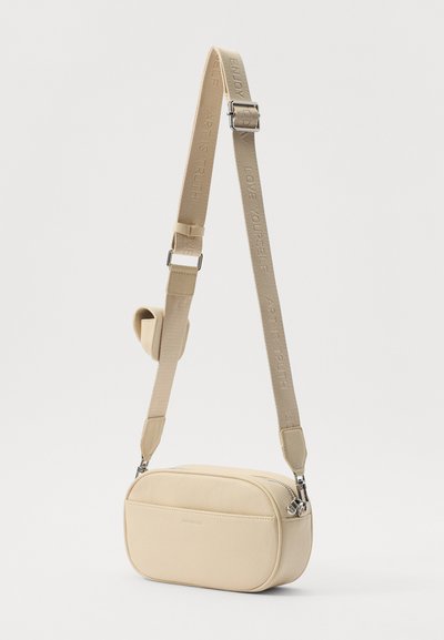 Beige crossbody bag with a structured rectangular shape, textured surface, and adjustable strap featuring embossed text. Silver hardware accents.