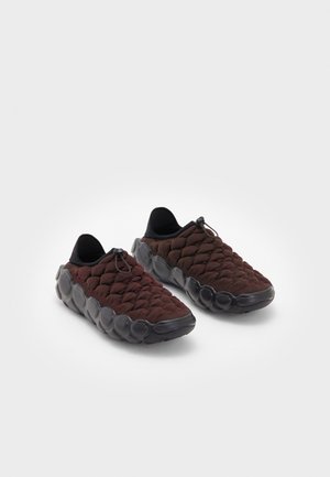 Ciemnobrązowe sneakersy typu slip-on z teksturowanymi dzianinowymi wierzchami i czarnymi podeszwami z wzorem bąbelków, wyposażone w regulowane elastyczne sznurówki.