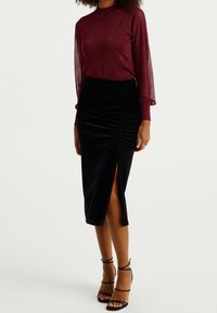 Mörkröd långärmad topp med genomskinliga texturerade ärmar, kombinerad med en svart sammetsmidikjol med rynkad effekt och ett framplock. Svarta remsandaler.