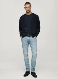 Marineblauwe cardigan, donker T-shirt, lichtblauwe jeans en zwarte schoenen. Cardigan heeft knopen; jeans hebben een vervaagd ontwerp. Eenvoudig, klassiek ontwerp.