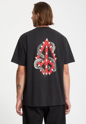 T-shirt en coton noir avec un design graphique audacieux en rouge et blanc représentant un serpent enroulé autour d'une forme abstraite.