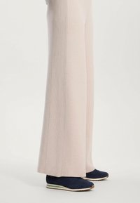 Világos rózsaszín, bő szárú nadrág, oldalsó varrásain bordázott textúrával, navy színű sportcipővel, fehér és zöld talppal párosítva.