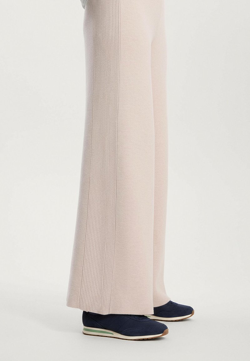 Világos rózsaszín, bő szárú nadrág, oldalsó varrásain bordázott textúrával, navy színű sportcipővel, fehér és zöld talppal párosítva.