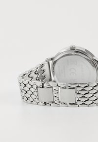 Montre en acier inoxydable argenté avec un bracelet à motif hexagonal et une boucle carrée. Boîtier rond à l'arrière avec des détails gravés.