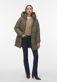 Olivengrønn isolert dunjakke med hette, med glidelåslukking foran, elastiske mansjetter og kort lengde, båret over en lys genser og mørke jeans.