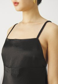 Czarna satynowa sukienka z cienkimi plecionymi ramiączkami, kwadratowym dekoltem i gładką fakturą. Minimalistyczny design bez widocznych zdobień.