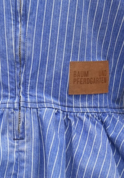 Ύφασμα με κάθετες ρίγες σε μπλε και άσπρο, με ορατό φερμουάρ και καφέ δερμάτινο ταμπελάκι με την ένδειξη "BAUM UND PFERDGARTEN".