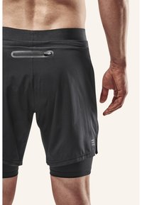 Zwarte sportshorts met een aansluitende onderbroek, elastische tailleband, een ritszak aan de achterkant en een gladde, lichtgewicht textuur.
