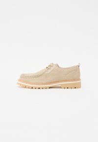 Chaussures en daim beige à lacets avec un bout arrondi, des coutures contrastantes et une semelle en caoutchouc beige robuste avec un motif texturé.