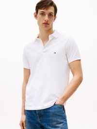 Hvid polo skjorte med krave, tre knapper og et lille, dekorativt logo. Sammen med blå denim jeans, vist fra livet og op.