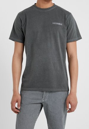 Man draagt een vervaagde zwarte T-shirt met korte mouwen met kleine witte tekst op de borst en zwart-witte verticale gestreepte broek.