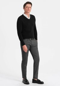 Schwarzer V-Ausschnitt-Pullover über einem weißen Kragenhemd, kombiniert mit grauen, maßgeschneiderten Hosen und schwarzen Schuhen, was ein elegantes, modernes Outfit ergibt.