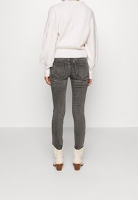 Jeans ajustados grises con bolsillos traseros, combinados con un suéter claro texturizado y botas de tobillo beige con tacón de madera.