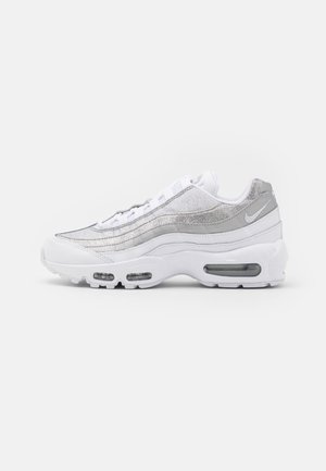 Valkoinen ja hopeanvärinen Nike Air Max 95 -lenkkitossu, jossa näkyvä ilmavaimennus ja kerroksittain aseteltu tekstiili- ja nahkapäällinen, kuvattuna sivuprofiilista.