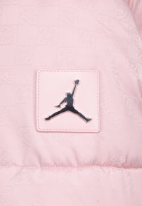 Różowa kurtka puchowa z teksturą z powtarzającym się wzorem "23", prostokątną naszywką z czarnym logo Jumpman wyraźnie widocznym.