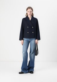 Marineblå dobbeltradet jakke med guldknapper, parret med lyseblå slidte funky jeans og en lille sort håndtaske. Glat stoftekstur.