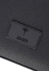 Portafoglio in pelle nera con texture, caratterizzato da una placca rialzata nera con il logo del marchio "JOOP!" e un design emblematico.