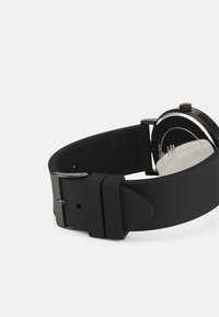 Schwarze Silikonarmbanduhr mit matter Oberfläche, ausgestattet mit einem Gehäuse in Silberfarbe und einer strukturierten Unterseite für besseren Halt. Verstellbarer Metallverschluss.